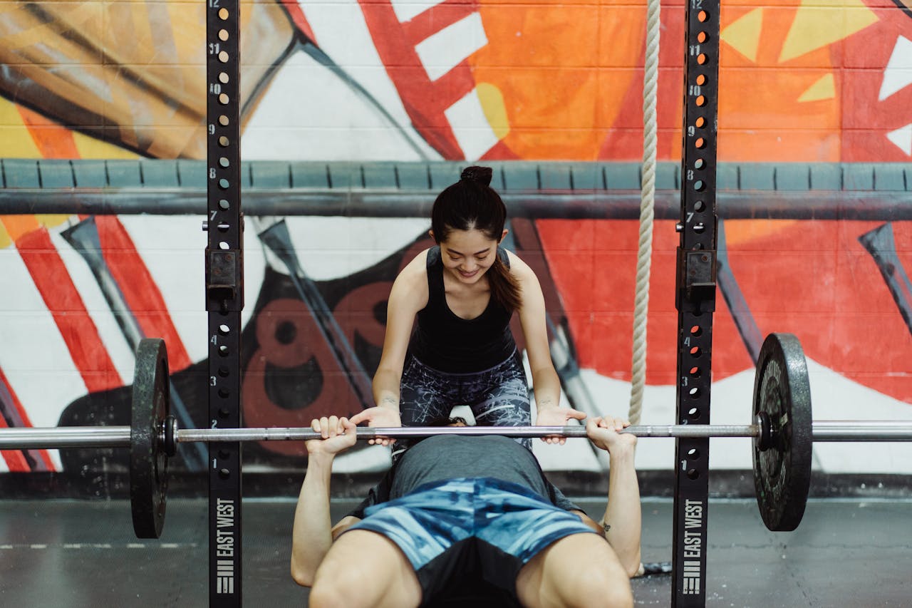 Crafting Captivating Headlines: Your awesome post title goes here Man lifting weights in gym assisted by woman with colorful mural background.